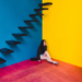 Sad woman sitting under stairs in colorful room