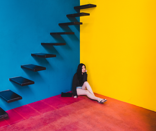Sad woman sitting under stairs in colorful room